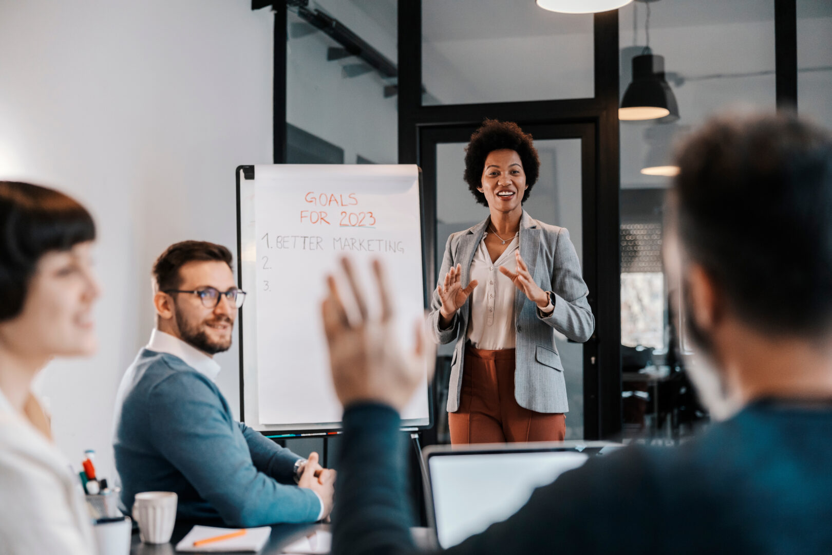 A multicultural businesswoman is standing next to a whiteboard and having brainstorming with her team at the office.
