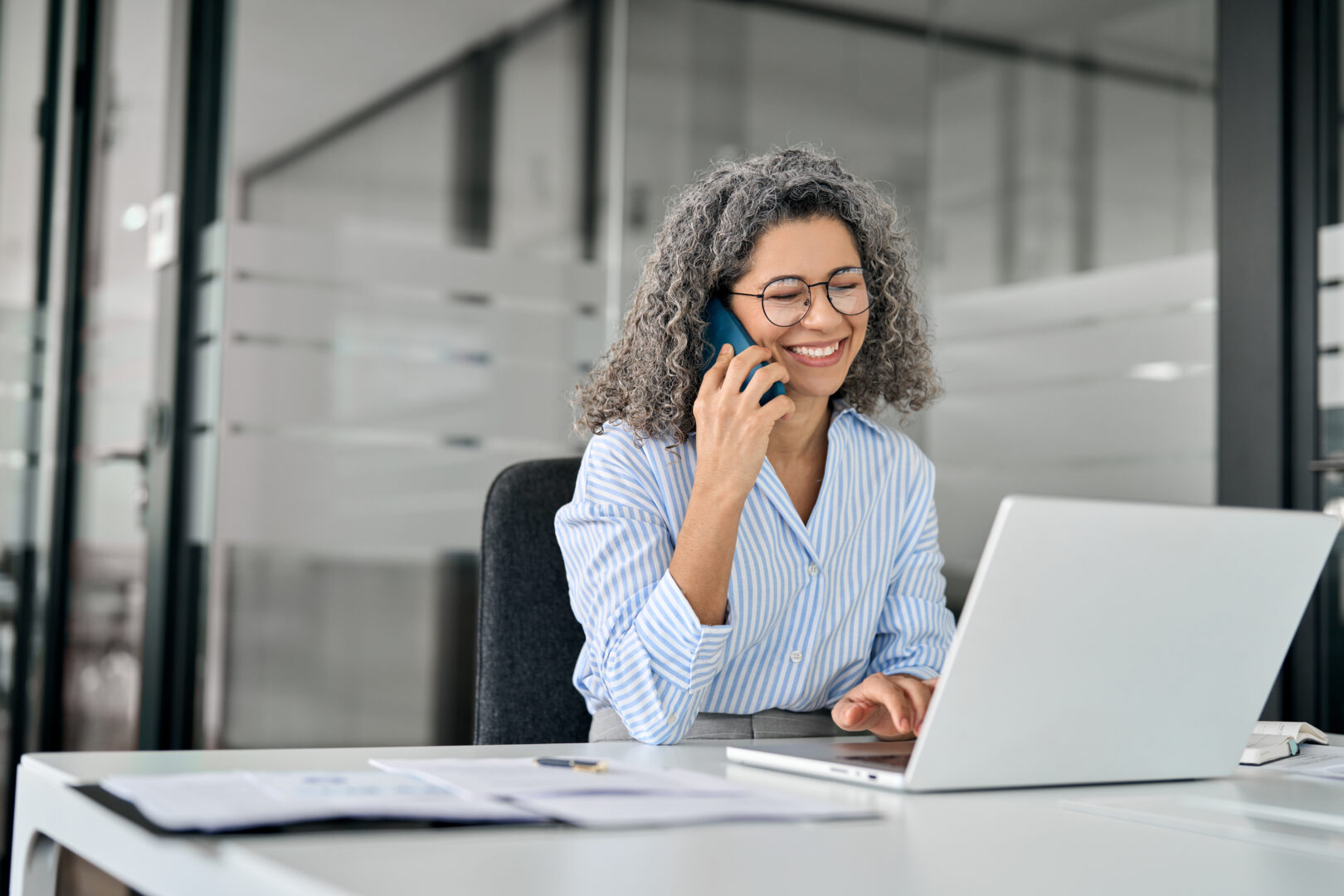 Smiling mature business woman talking on phone making business call in office.